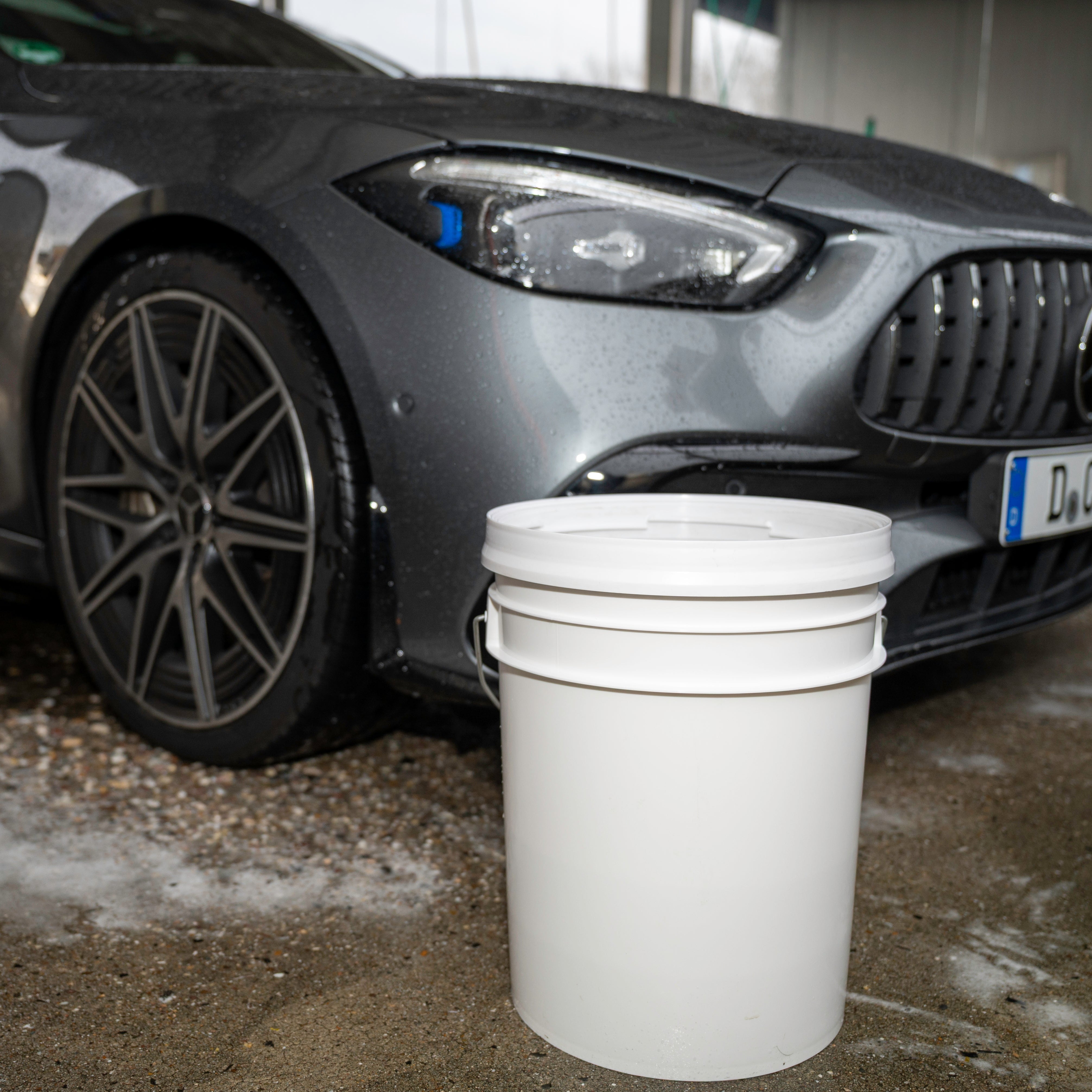 Car parked next to a white bucket on a concrete surface