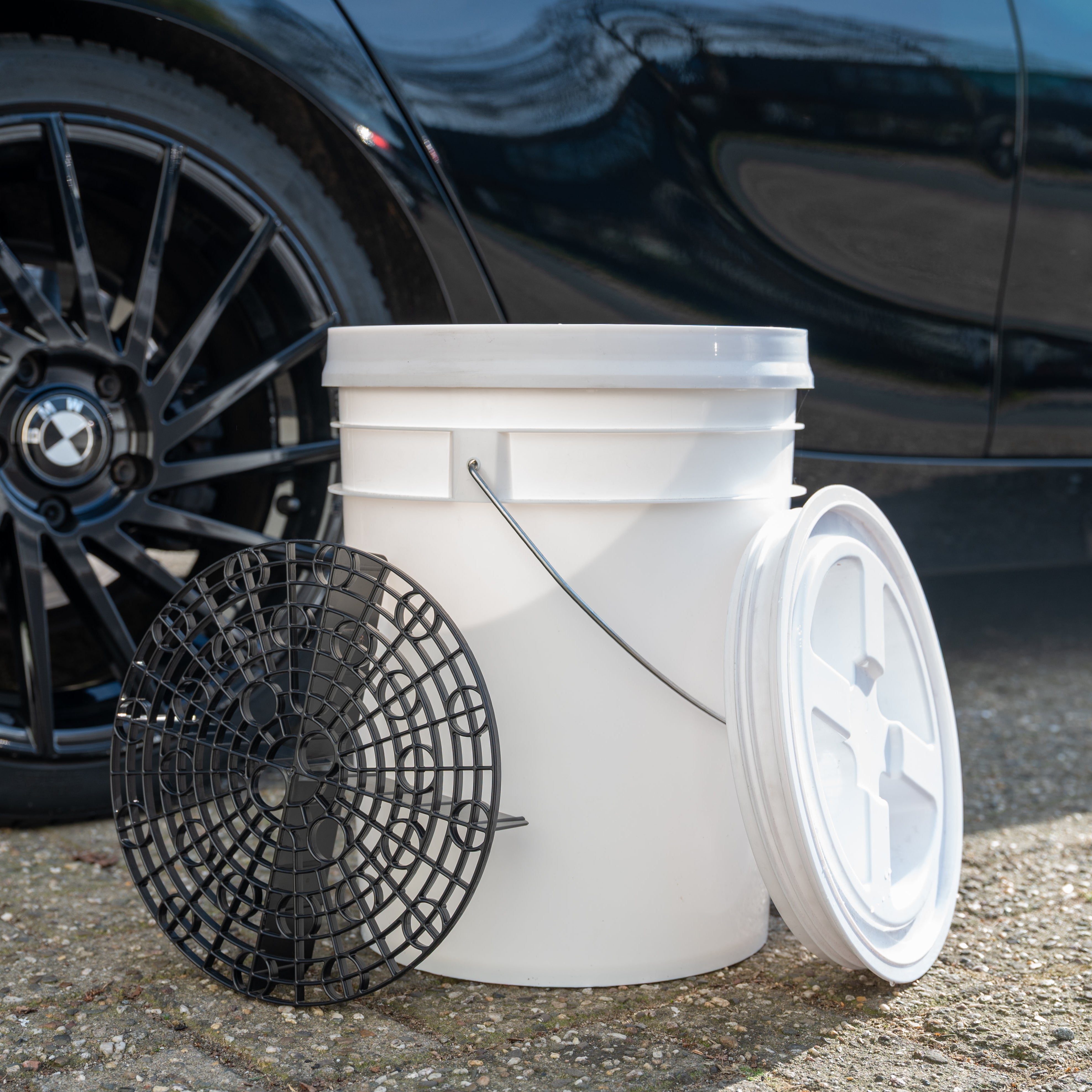 White bucket with a black grit in front of a black BMW car.