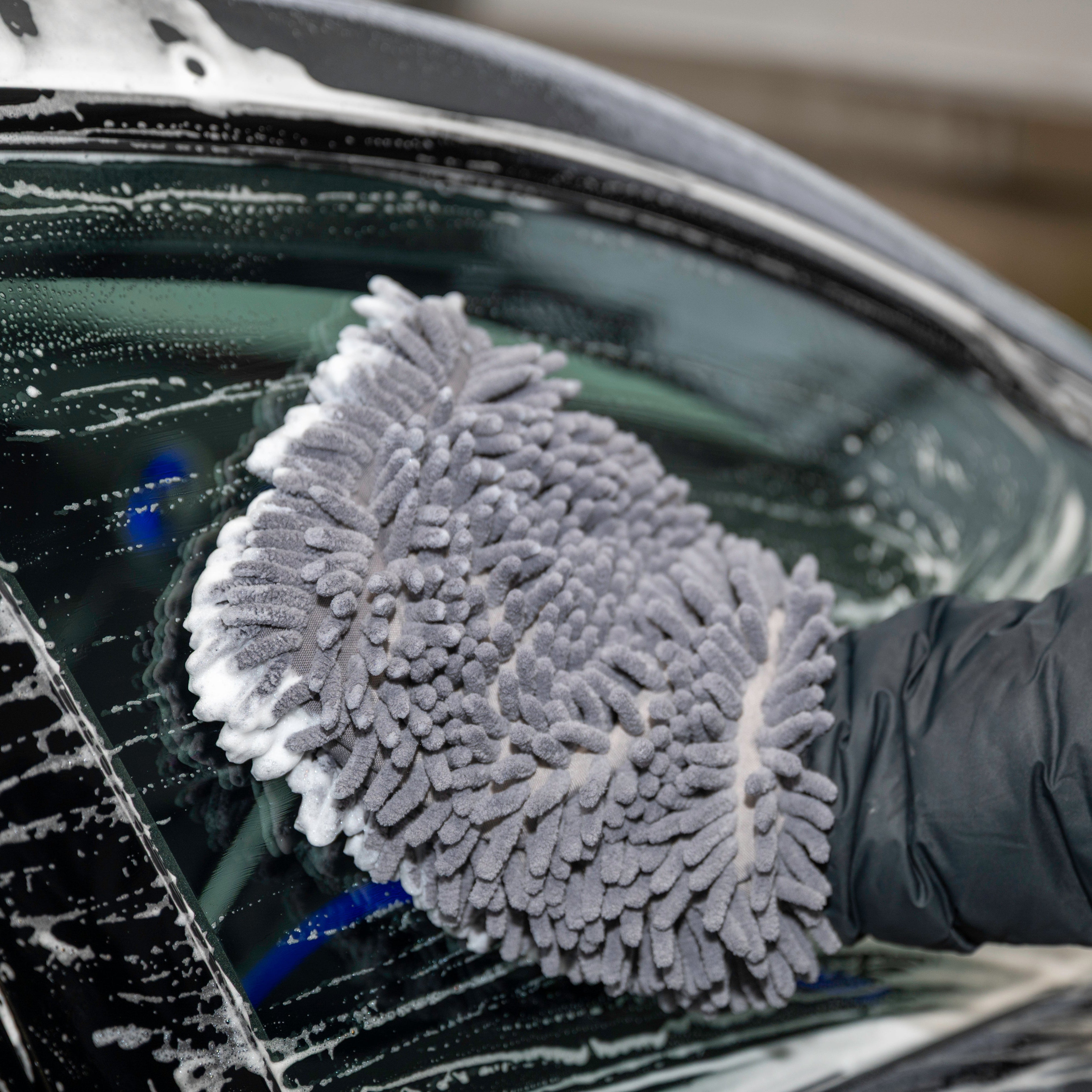 Person cleaning a car window with a gray microfiber glove