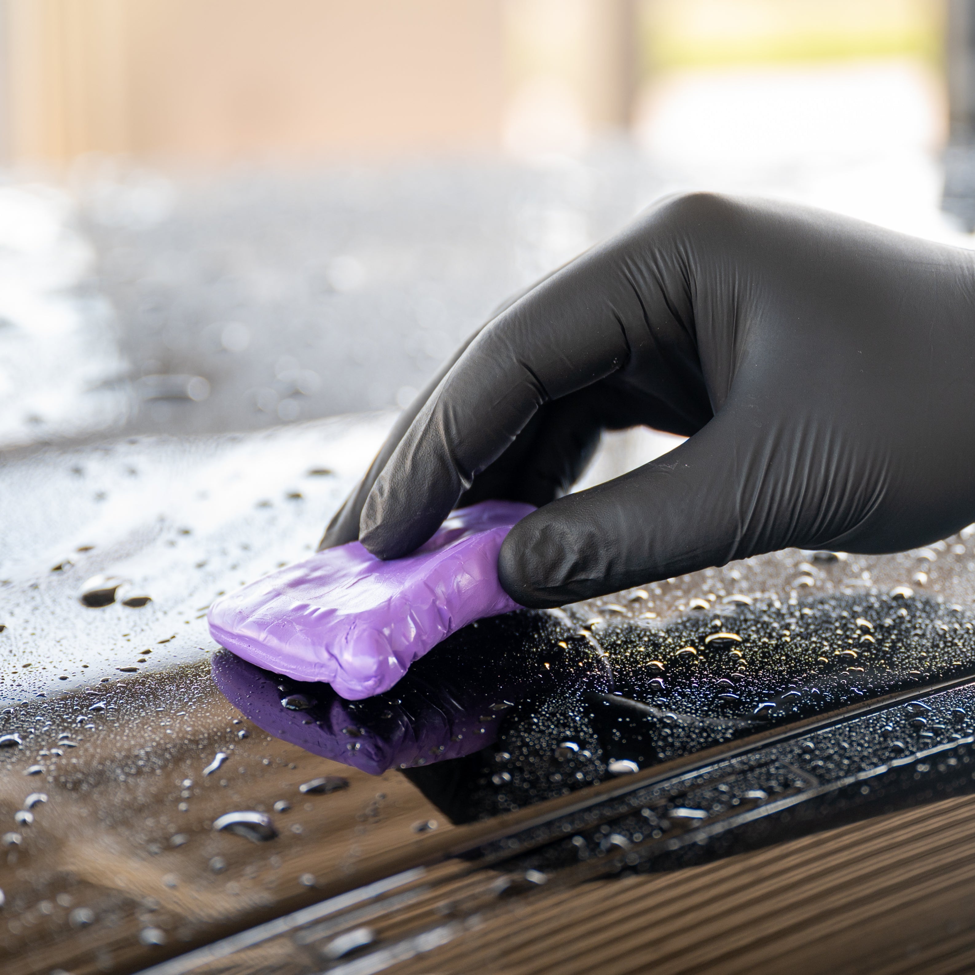Person cleaning a car with a purple Clay Bar and black gloves.