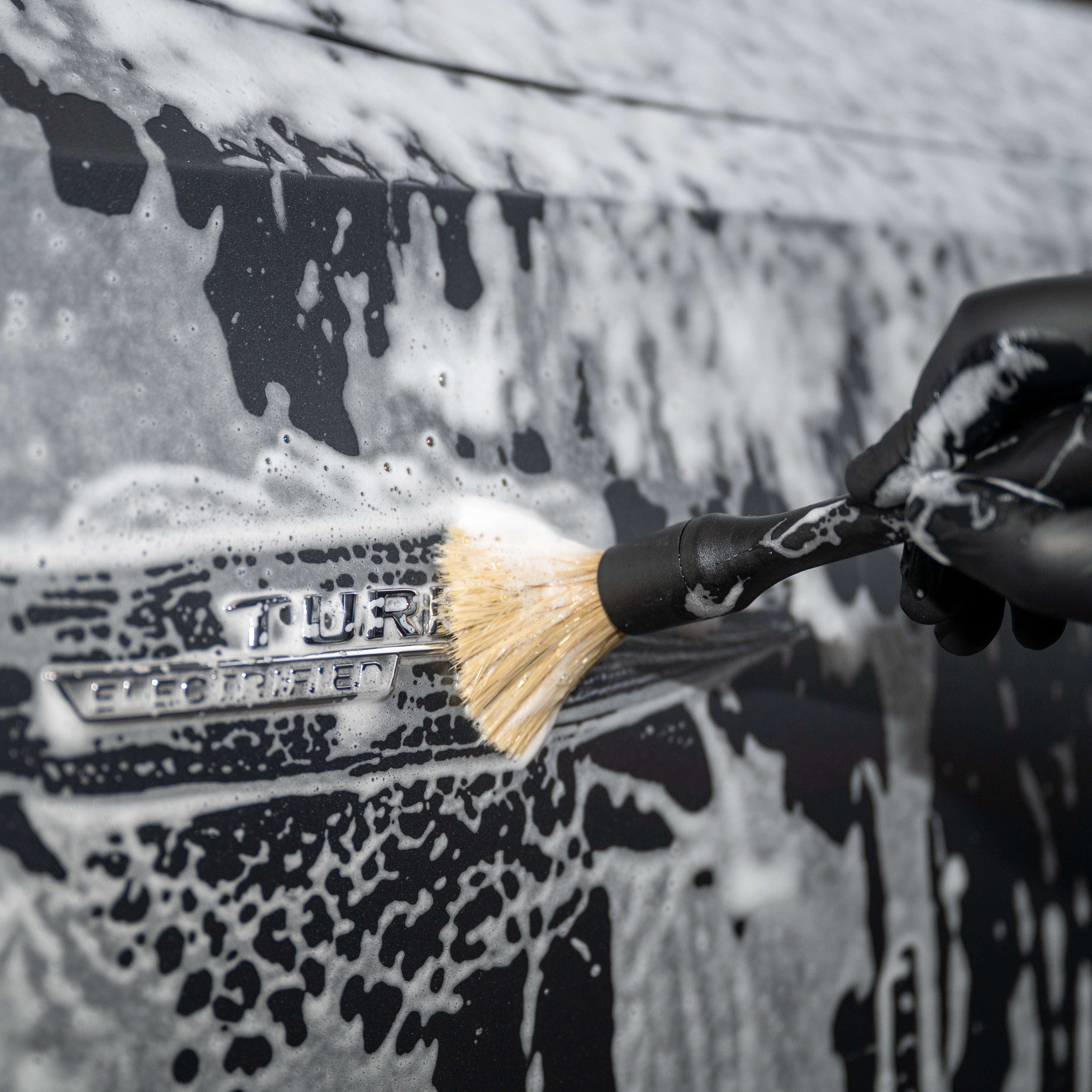 Person cleaning a car with a brush, wearing black gloves