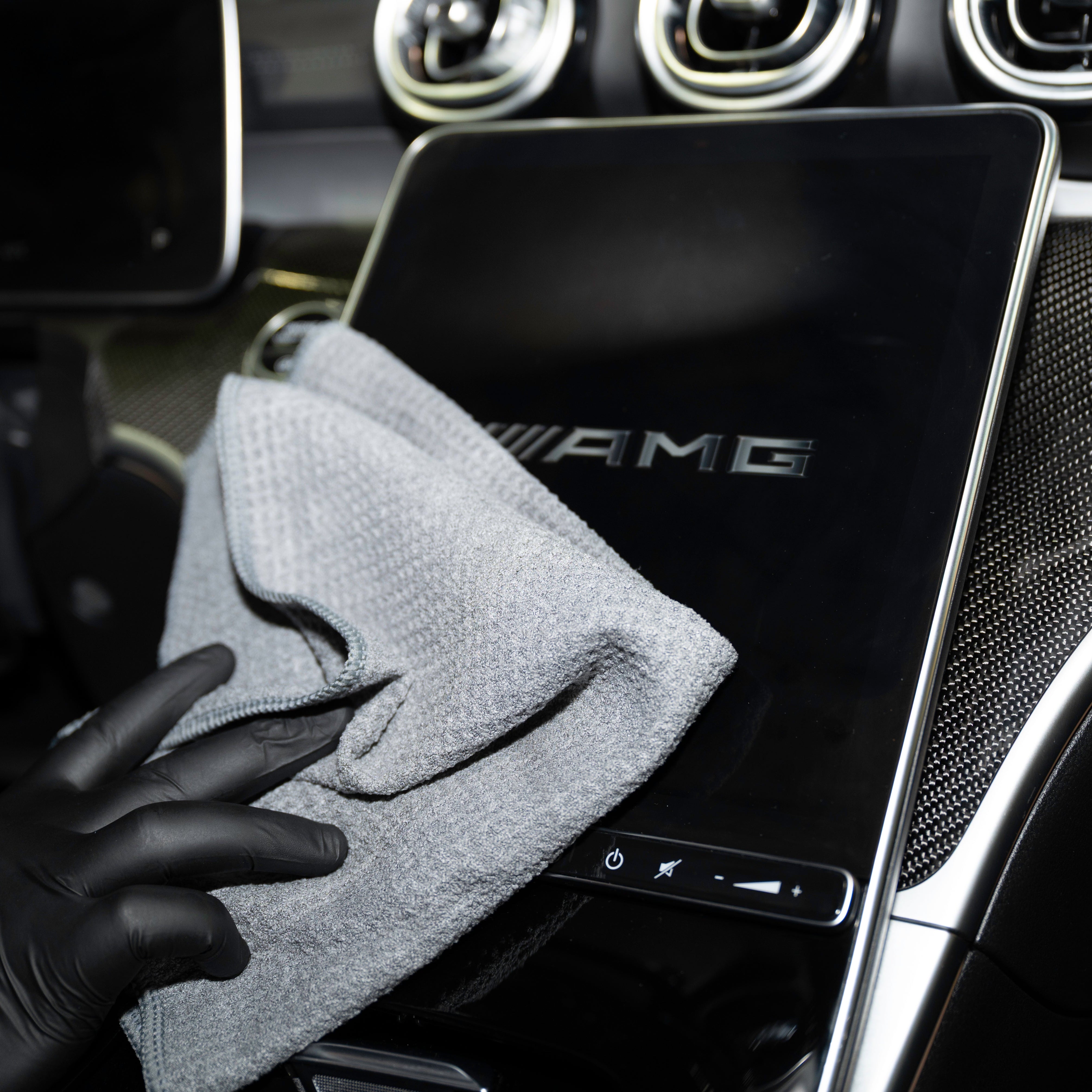 Person cleaning a car's digital display with a microfiber cloth, with 'AMG' branding visible.
