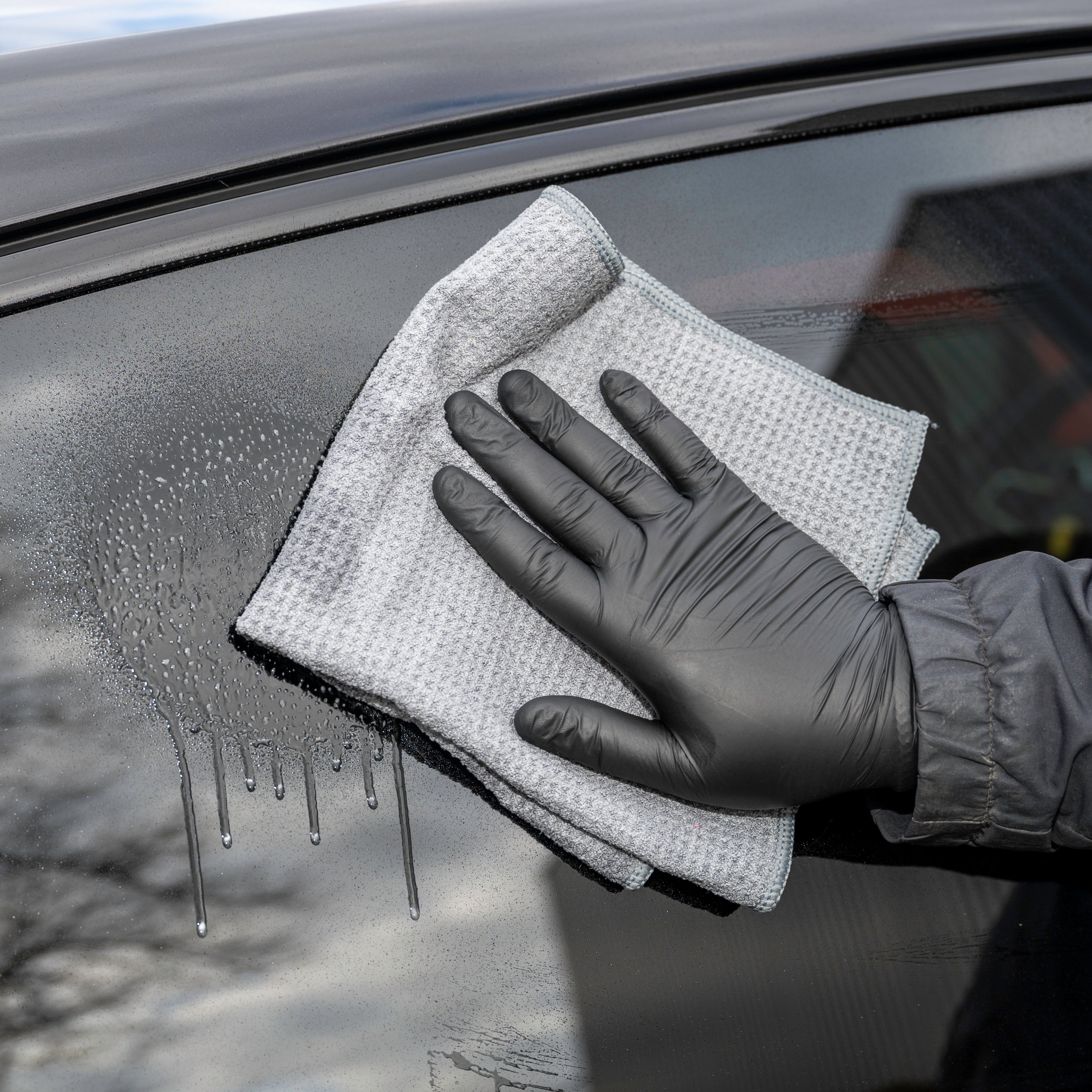 Person cleaning a car window with a microfiber cloth and black gloves.
