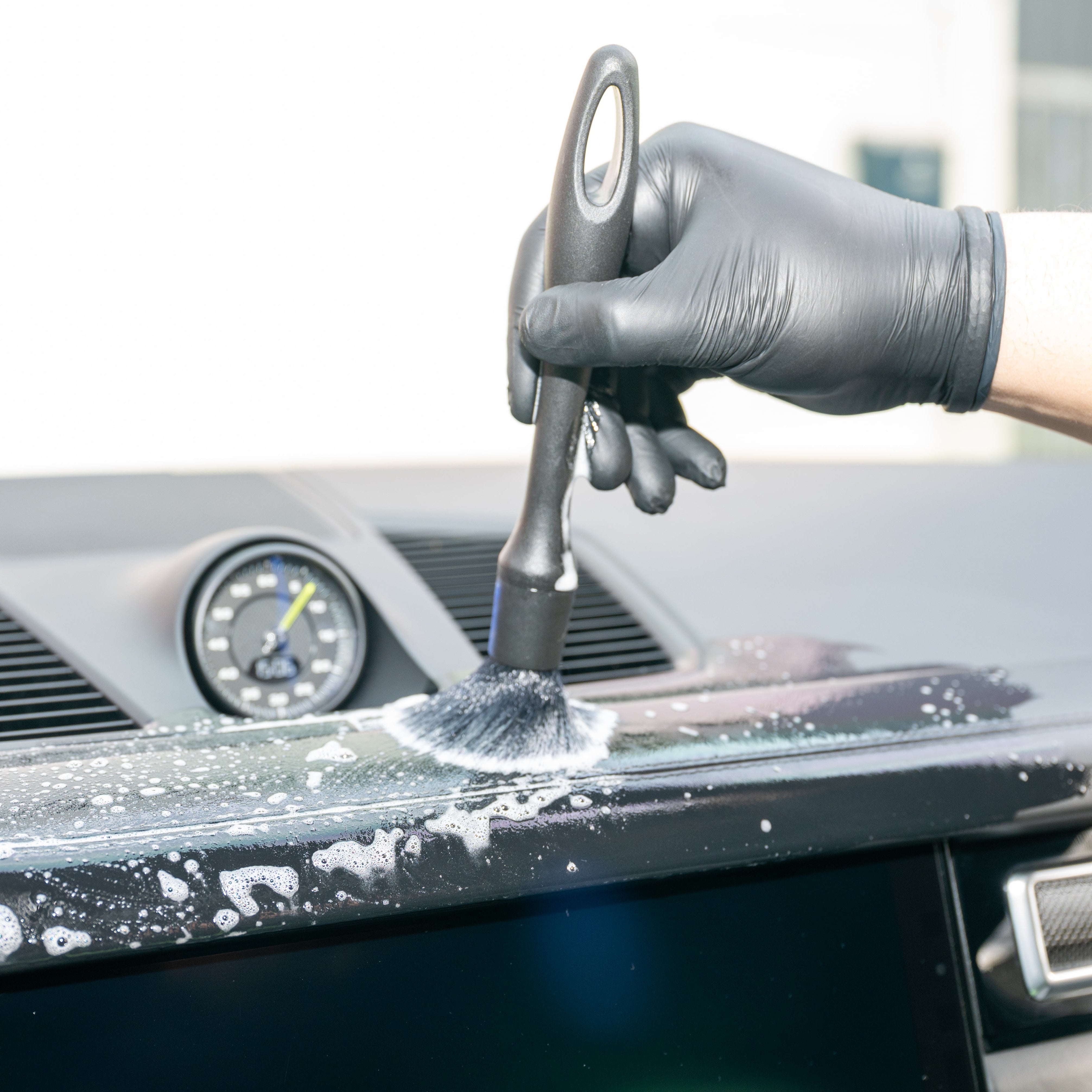 Person cleaning a car's dashboard with a brush and soap solution.