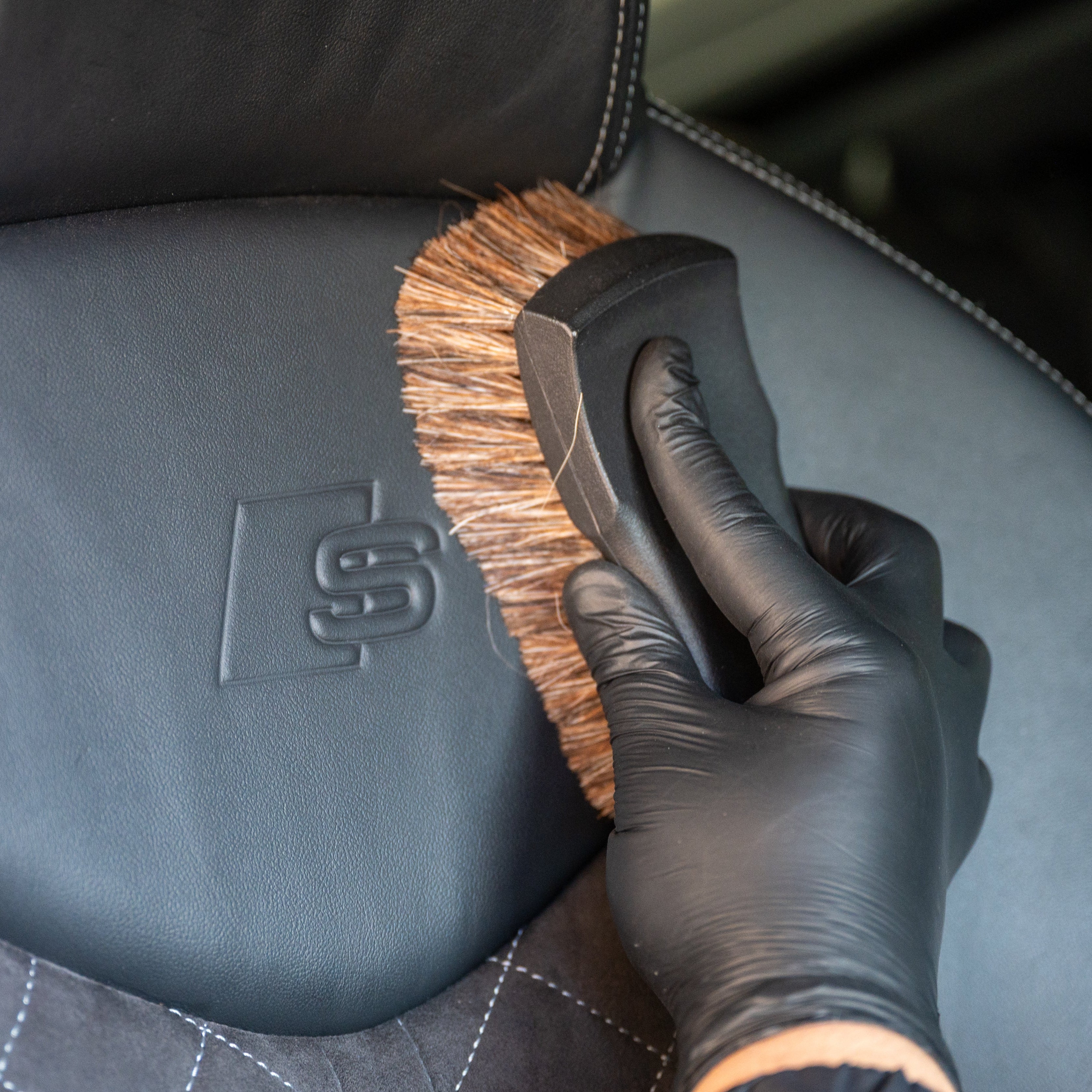 Person cleaning a car seat with a brush, wearing black gloves.