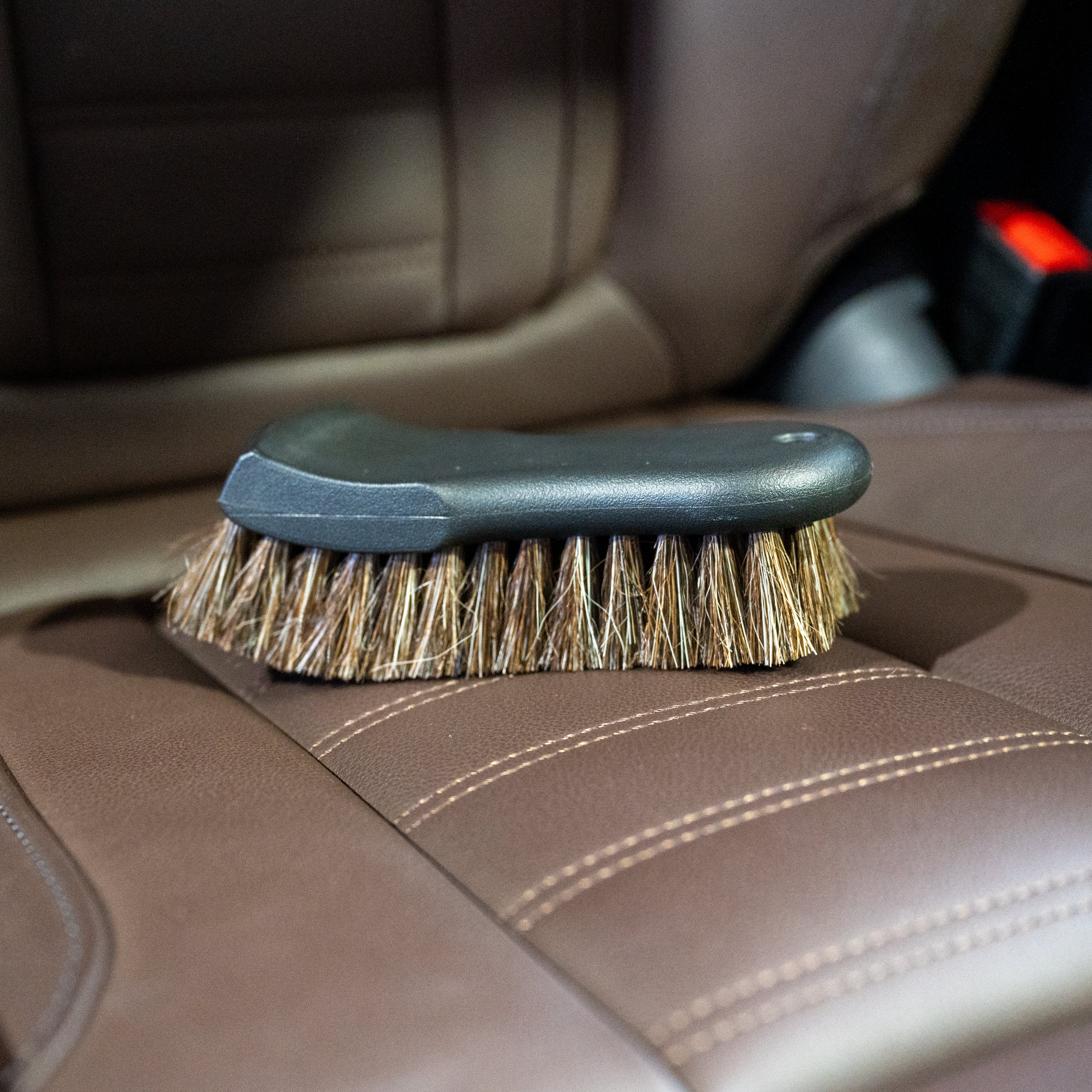 Car interior cleaning brush on a brown leather car seat