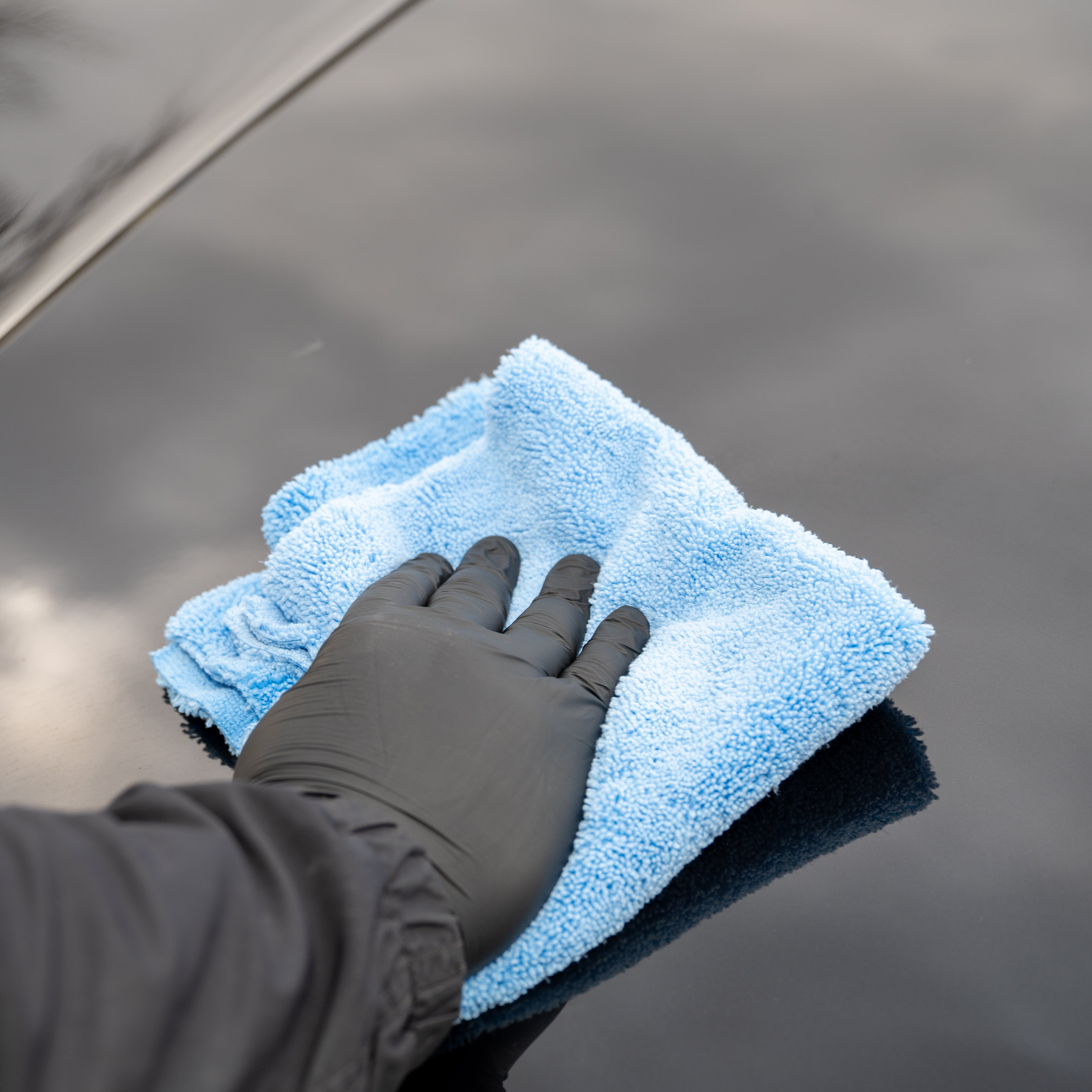 Person cleaning a car window with a blue microfiber cloth and black glove.