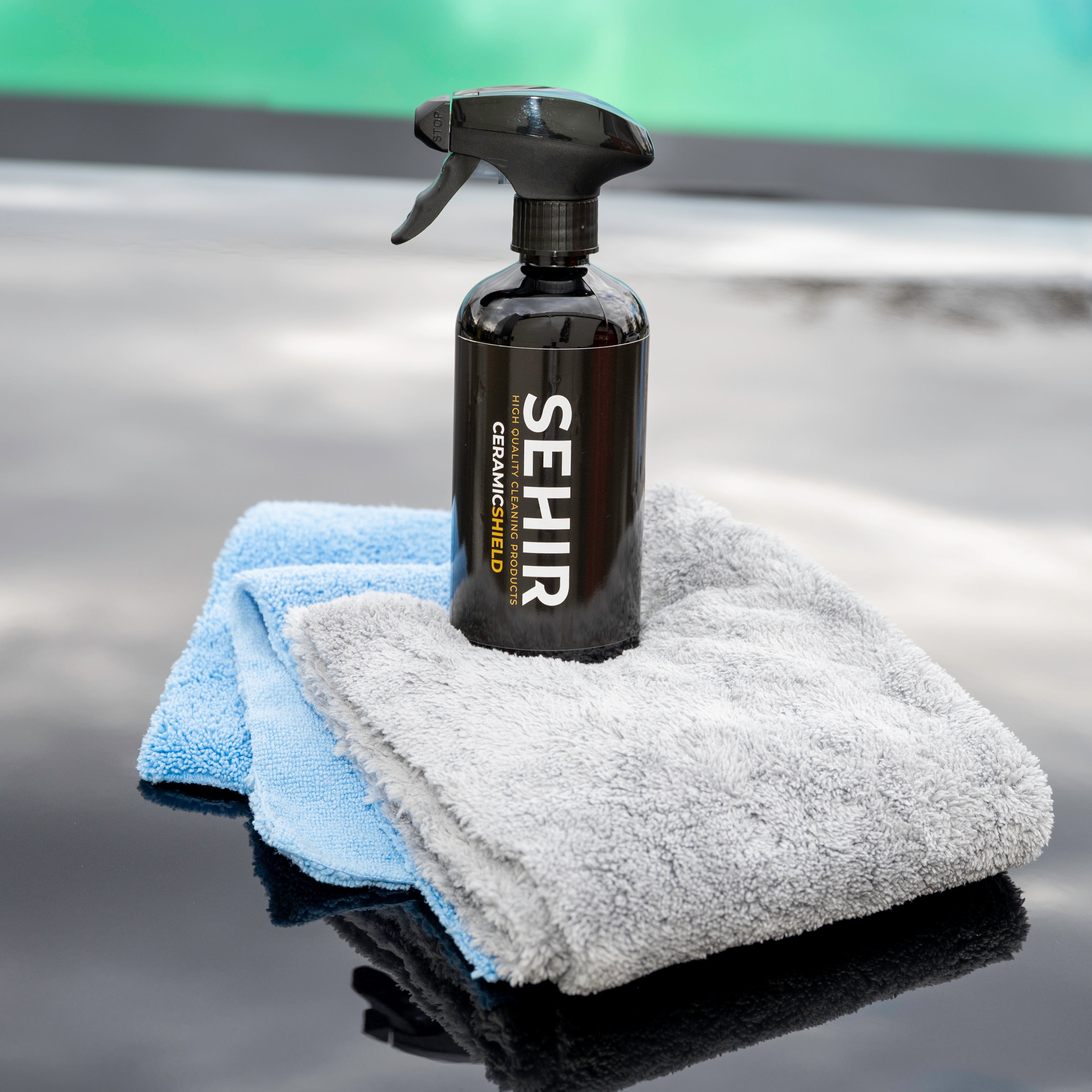 Spray bottle and cloths on a reflective surface with 'SEHIR' branding.