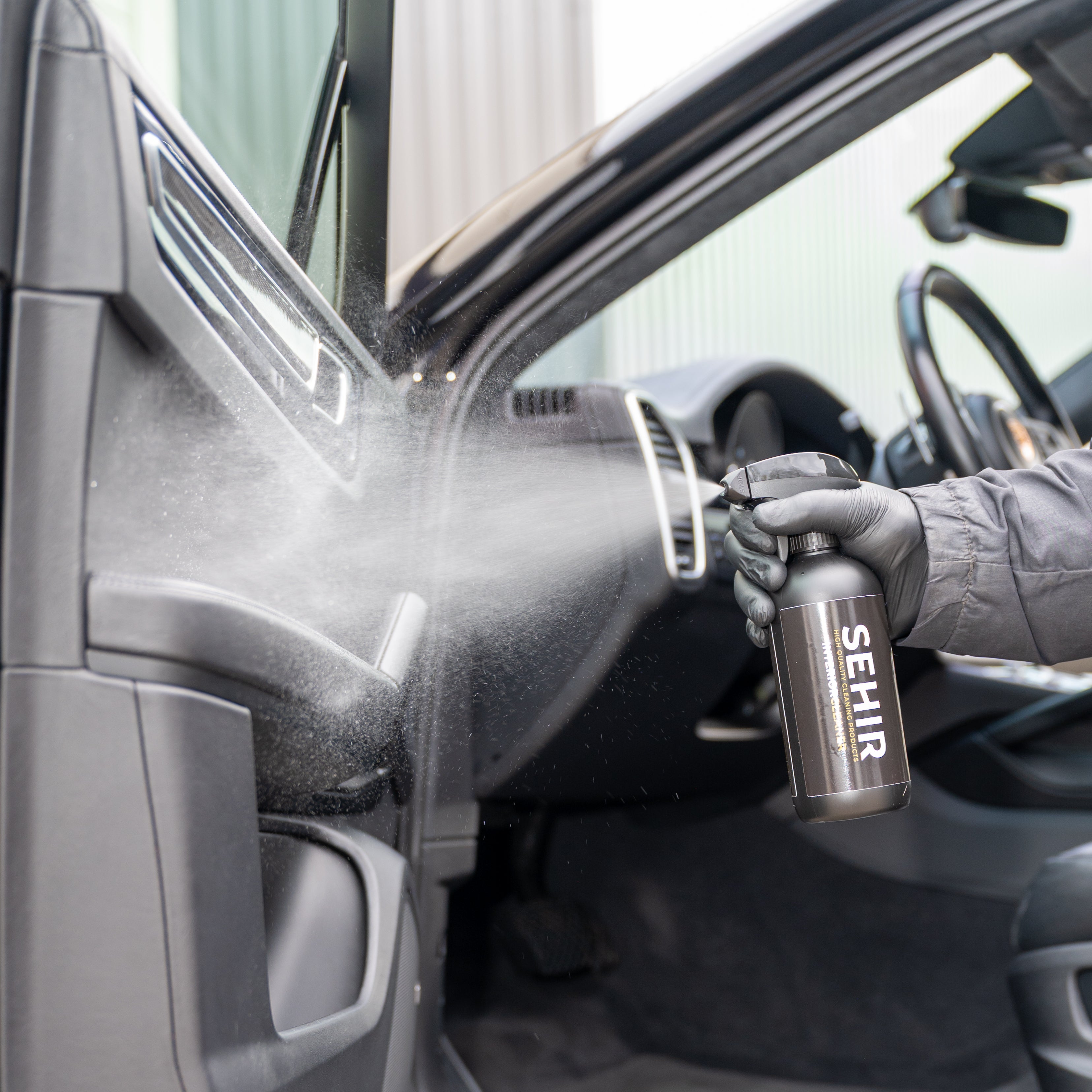 Person cleaning car interior with a spray bottle labeled 'SEHIR'.