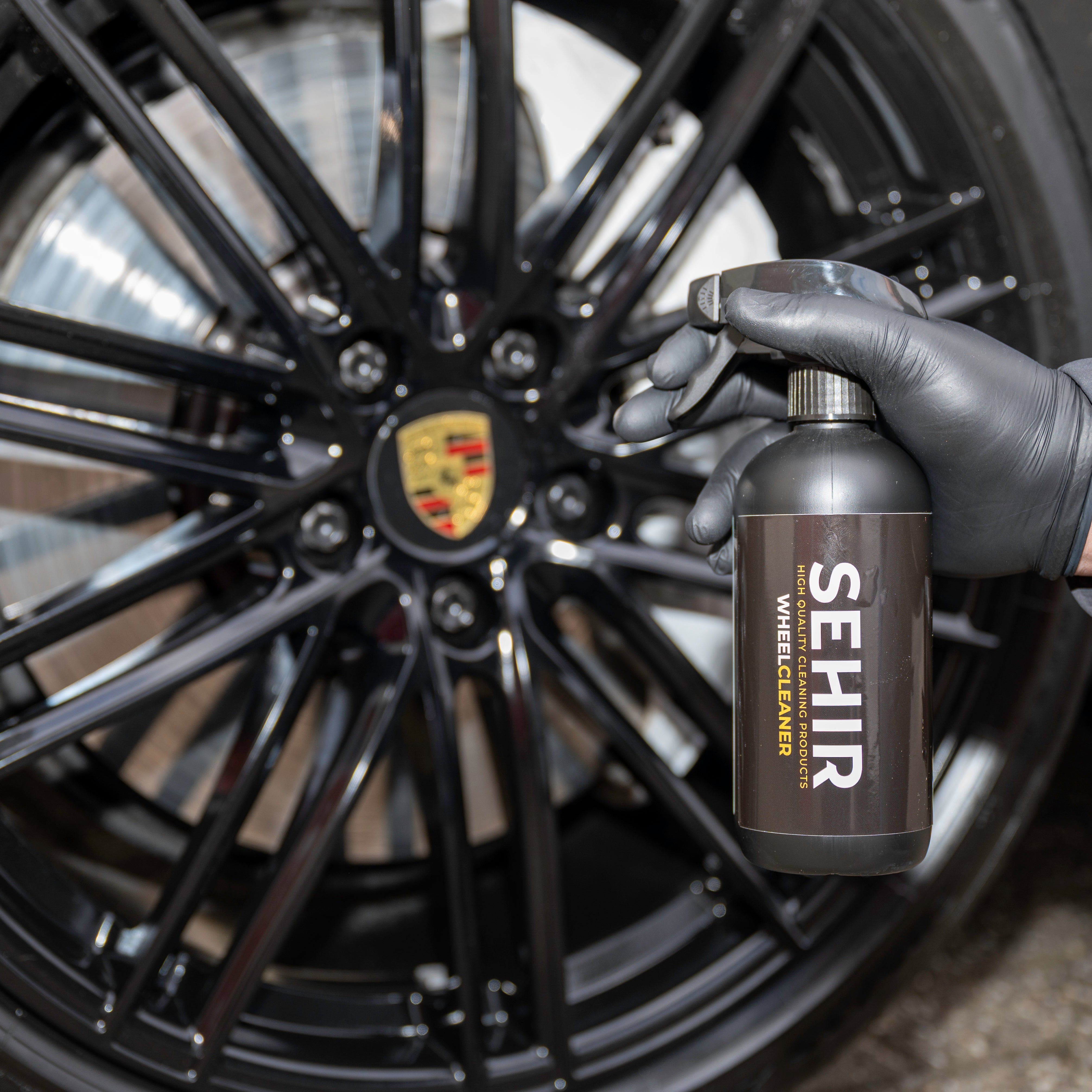 Person holding a bottle of SEHIR wheel cleaner next to a car wheel with a Porsche logo.