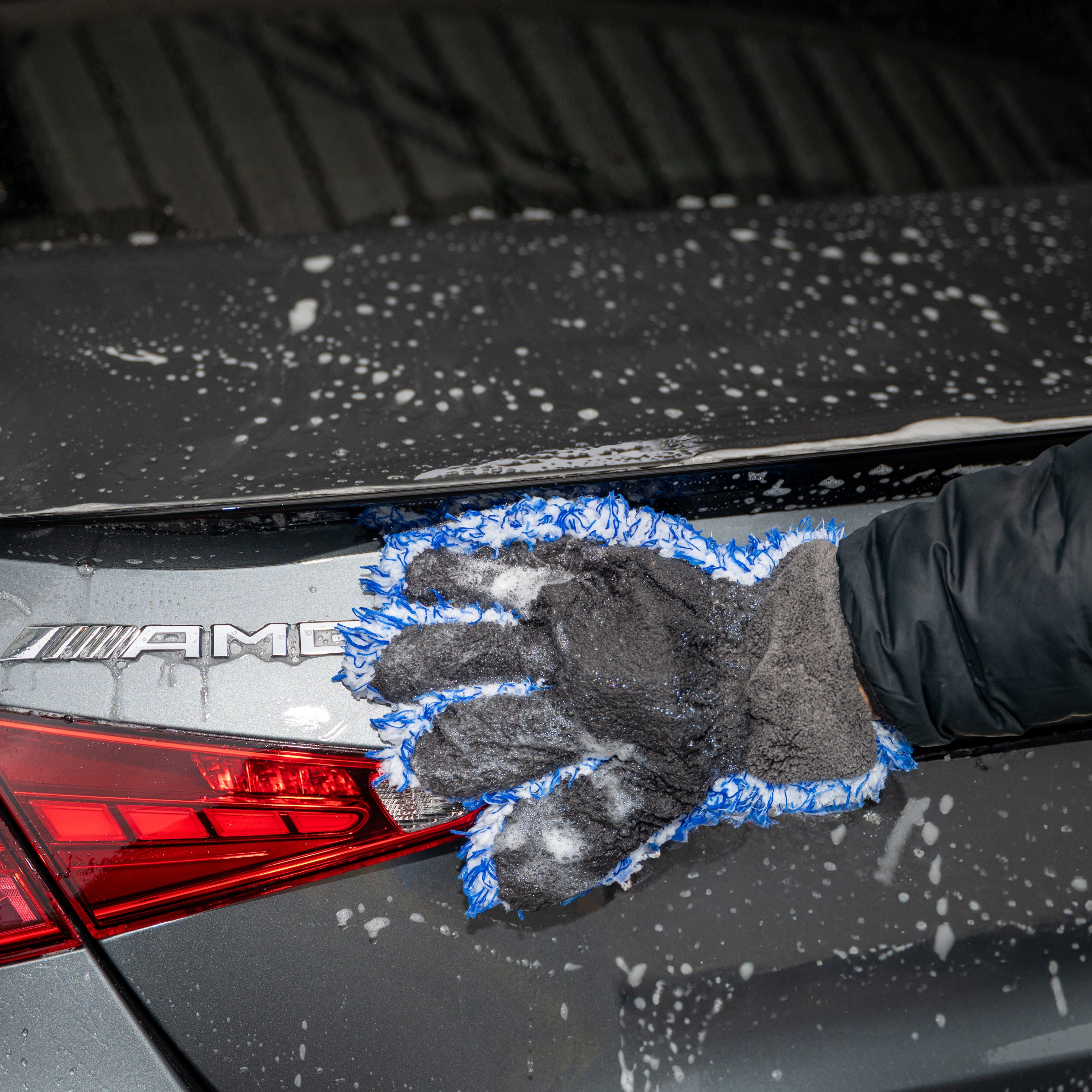 Person cleaning a car's trunk with a blue sponge, featuring an AMG logo.