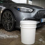Car parked next to a white bucket on a concrete surface 