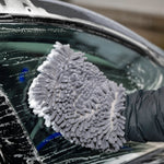 Person cleaning a car window with a gray microfiber glove