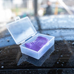Purple Clay Bar in a clear plastic case on a wet surface