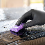 Person cleaning a car with a purple Clay Bar and black gloves.