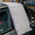 Person cleaning a car window with a gray towel