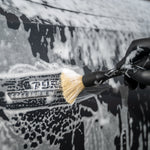 Person cleaning a car with a brush, wearing black gloves