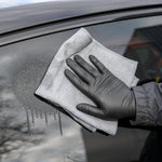 Person cleaning a car window with a microfiber cloth and black gloves.