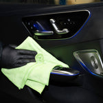 Person cleaning car interior with a green cloth and black gloves