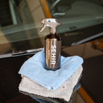 Spray bottle labeled 'SEHIR' with cloths on a car window