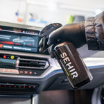 Person holding a can of SEHIR car care product inside a vehicle.