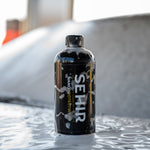 Black bottle labeled 'SEHIR' on a textured surface with a blurred background