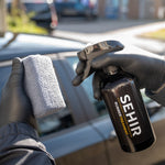 Person holding a spray bottle labeled 'SEHIR' and a sponge in front of a car.