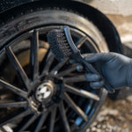 Person cleaning car wheel with a brush, wearing a blue glove.